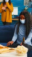 Multiethnical women playing backgammon wearing face mask as prevention for covid 19 spread during global pandemic sitting on sofa drinking beer and eating popcorn. Enjoying board games in outbreak photo