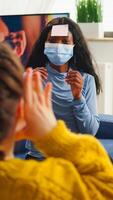Mixed race of people with sticky notes on foreheads playing name game having fun with beer and popcron keeping social distacing. with face mask to prevent spread of covid19 in home living room. photo