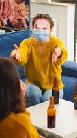 Funny friends with sticky notes on foreheads enjoying name game gesturing during new normal party wearing face mask keeping social distancing preventing covid19 spread. People enjoying bottles of beer photo