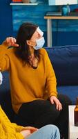 Happy cheerful multi ethnic friends with face mask playing games with sticky notes on forheads drinking beer eating popcorn guesing keeping social distancing. during outbreak in home living room photo