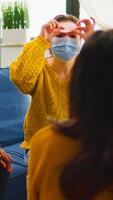 Happy woman with sticky note on forehead playing name game with multiethnic friends keeping social distancing drinking beer in home living room due to social pandemic. People having fun in outbreak photo