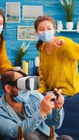 Group of multi ethnic friends with face mask enjoying playing games using vr headset goggles in living room keeping social distancing agaist covid19. Diverse people having fun at new normal party photo