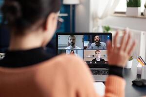 Student in a group videocall on laptop. Freelancer working from home office meeting colleagues online. Colleague waving at screen in webcam team conference. Remote briefing conversation. photo