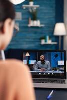 Freelancer with laptop in a videocall with client. Over the shoulder view of student attending online lesson with teacher from home. Man talking in online webinar conference. photo