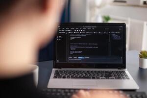 Freelancer writing code on laptop using keyboard. Freelance student programmer working remote developing software. Software coder looking for errors in home office. Code tester debugging. photo