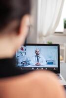 Student working from home videocalling doctor on laptop. Over shoulder view of freelancer in online medical consultation call. Physician gives health advice on webcam. photo