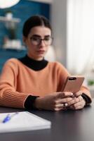 Content creator holding smartphone looking at content on screen. Student with glasses reading email on smart phone. Freelancer looking concerned while watching important text on mobile display. photo