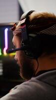 Focused man gamer putting headset playing shooter online game on RGB powerful computer in living room late night. Pro cyber streaming gaming championship, participating in eSports tournament photo