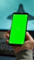 Competitive gamer looking at smartphone with green screen chroma key desktop playing online games on powerful computer during live tournament. Cyber player using phone with mock up isolated display photo