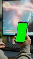 Concentrate gamer holding phone with green screen mock up chorma key display while playing games on powerful computer streaming online competition. Player using isolated desktop playing shooter games photo