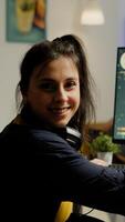 Woman gamer with headset looking at camera smiling and playing virtual shooter game championship in cyberspace, esports player performing on powerful computer in stylish room during gaming tournament photo