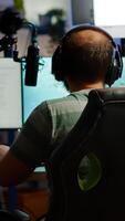 Back shot of streamer man playing on powerful computer shooter game for tournament, talking with multiple players into headphones. Pro game r using professional streaming equipment photo