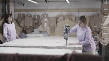 Two professional seamstresses are operating a fabric cutting machine in a workshop video