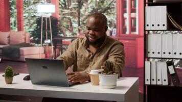 Successful entrepreneur using his laptop for remote business operations, demonstrating effective telecommuting strategies. Focuses on development and project management at home office. Camera A. video
