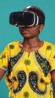 Vertical Gorgeous girl in ethnic clothes using vr glasses against blue background, working with high tech 3d experience with virtual reality device. Young woman using smart headset. Camera A. video