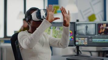 Black videographer wearing VR headset editing project in production studio office. maker employee processing film montage in digital multimedia company while, colleagues working in background video