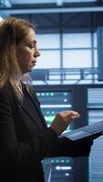 Vertical Woman walking in high tech facility, using laptop to patch network issues leading to slow data transfer rates. Employee in data center fixing errors affecting servers performance, camera A video
