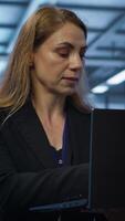Vertical Engineer doing yearly checkup to prolong data center electronics life span and avoid downtime. Woman in server room monitoring server infrastructure components using laptop, camera A video