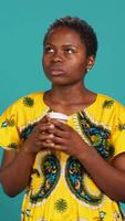 Vertical Young smiling person enjoying freshness of coffee cup in studio, drinking caffeine refreshment and relaxing against blue background. Happy woman serving a fresh beverage. Camera A. video