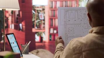 Entrepreneur analyzing architectural sketches and blueprints at his home, planning the layout and design of a new office to foster business development. Hunting for creative workspace. Camera A. video