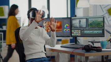 African editor experiencing VR goggles, gesturing, editing film montage working with footage and sound on computer with two displays. Videographer processing movie in creative agency video