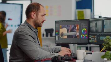 Videographer looking at camera smiling working in creative startup workplace using editing post production software on professional pc with two monitors, processing editing film footage. video