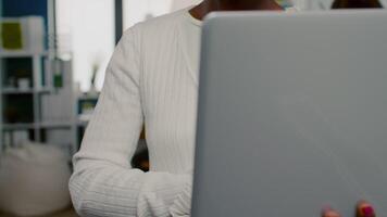 Close up of african woman looking at camera smiling standing in start up creative agency office holding laptop, typing on it. Black videographer editing project using post production software video