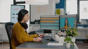 Satisfied photo editor retouching image using stylus pen, working on PC with dual monitors setup. Woman retoucher editing assets in pro software app with graphic tablet sitting in creative agency video