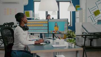 Black retoucher woman analysing images on pc with two monitors and retouching digital assets with stylus pencil. African project designer using photo editing software sitting in creative agency office video