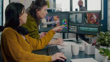 Art director explaning to woman videographer the steps for prosessing film montage, pointing on pc, writting on sticky notes. editor working in post production software in creative agency video