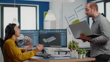 Man project supervisor holding laptop and talking with woman industrial engineer who works on computer the development of new machinery prototype. Diverse team working in creative agency office video