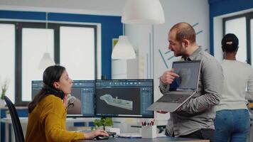 Man project supervisor holding laptop and pointing on display showing to woman industrial engineer who works on computer the development of new machinery prototype. Team working in creative office video
