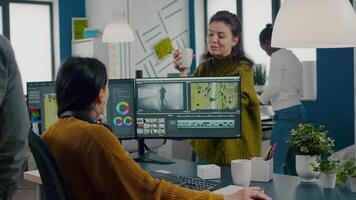 Team of videographers talking about project while working in editing app at computer with dual monitors setup sitting in modern digital multimedia company. Creatice women prosessing film montage video