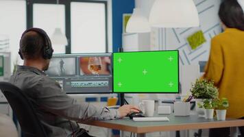 Videographer using computer with chroma key, mock up isolated display editing and audio footage. Man editor processing film montage on pc with green screen while team working in background video