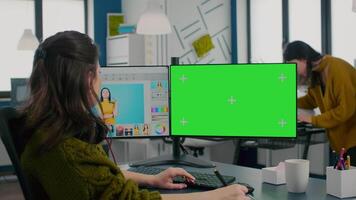 Photographer working on green mock-up screen, computer with chroma key, isolated display while sitting at desk retouching woman portrait in photo editing software. Retoucher looking at greenscreen video