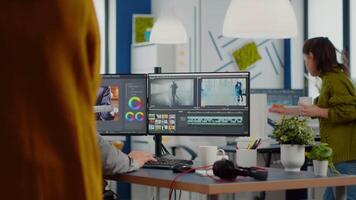 Videographer edits project and cuts footage and sound using post production software and two monitors taking notes. Man processing film montage in digital multimedia star up company video