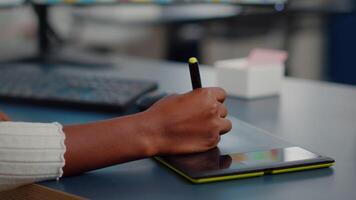 Close up on hand of african photo editor drawing on graphic tablet editing customer photo on computer with two monitors. Black retoucher holding stylus pen retouching assets in creative agency office video