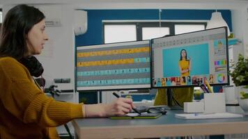 Photo editor using image editing software, retouching photos with color grading app sitting in start up creative agency office. Graphic designer using stylus pencil and computer with two displays. video