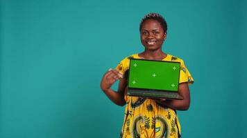 Confident happy person posing with a copy space mockup on laptop, create an advertisement with isolated display in studio. Young woman in ethnic attire with floral elements. Camera B. video