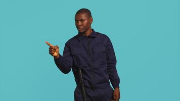 Portrait of security guard pointing finger at intruders while overseeing premises. Private law enforcement worker scolding unwanted trespassers, studio backdrop, camera B video