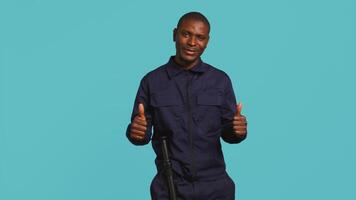 Portrait of joyous security guard doing thumbs up sign gesturing with finger while overseeing premises. Private law enforcement worker doing positive hand gesture, studio backdrop, camera B video