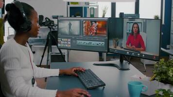 African woman editor with headset talking during online conference with partner on call editing client work, getting feedback on commercial movie using post production software on pc in office video