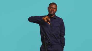 Portrait of security agent doing thumbs down sign gesturing, refusing entry while securing assigned post, studio background. Guardian doing negative hand gesture, handling security breaches, camera B video
