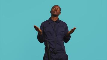 Security guard tasked with restricting unwanted access looking to sky, praying. Portrait of bodyguard waiting for miracle, doing spreading arms gesture, studio background, camera B video