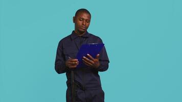 Security guard holding clipboard, taking notes, receiving orders during protection job shift. Portrait of bodyguard using pen to write informations received, studio background, camera B video