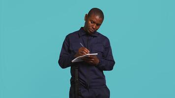 Security guard with notepad taking notes, receiving orders about suspects to look out. Portrait of bodyguard using pen, documenting layout location in need of protection, studio background, camera B video