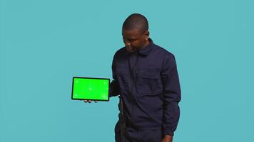 porträtt av säkerhet ombud presenter krom nyckel läsplatta och säkring tilldelad posta, studio bakgrund. väktare poäng finger till isolerat skärm enhet medan hantering säkerhet överträdelser, kamera b video