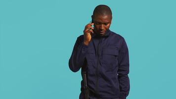 säkerhet vakt använder sig av mobiltelefon till göra ring upp till vänner under skydd jobb flytta. porträtt av livvakt i telefon ring upp med mates på arbete använder sig av telefon, studio bakgrund, kamera b video