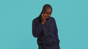 portrait de Sécurité garde à travail en utilisant téléphone à faire appel à copains tandis que surveillance locaux. privé loi mise en vigueur ouvrier dans Téléphone appel avec les amis, studio toile de fond, caméra b video