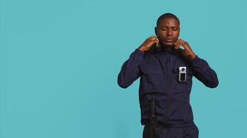 Security guard equipped with bodycam listening music, taking break from job shift. Portrait of bodyguard walking around perimeter with headphones on while at work, studio background, camera B video
